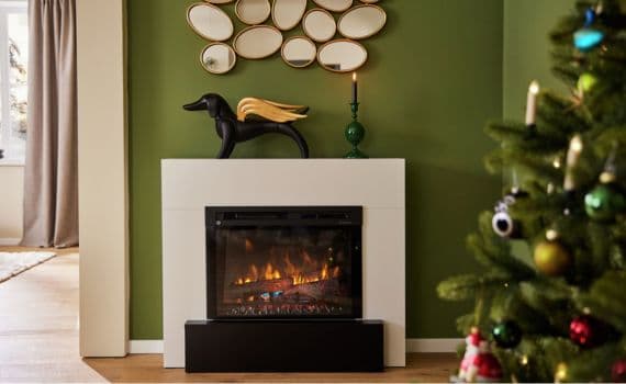 Elektrischer Kamin mit Flammen, grüne Wand, schwarzer Hund mit goldenen Flügeln, Spiegel, Weihnachtsbaum rechts