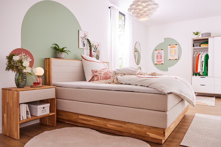 Helles und modernes Schlafzimmer mit einem beigen Boxspringbett, einem Nachttisch aus Holz und dekorativen Wandbildern.