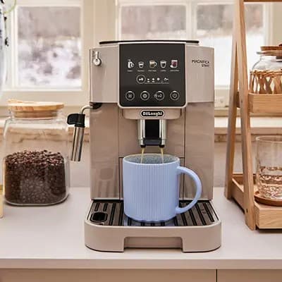 Kaffeevollautomat auf Küchenarbeitsplatte brüht Kaffee in eine große hellblaue Tasse vor Fenstern und Vorratsgläsern