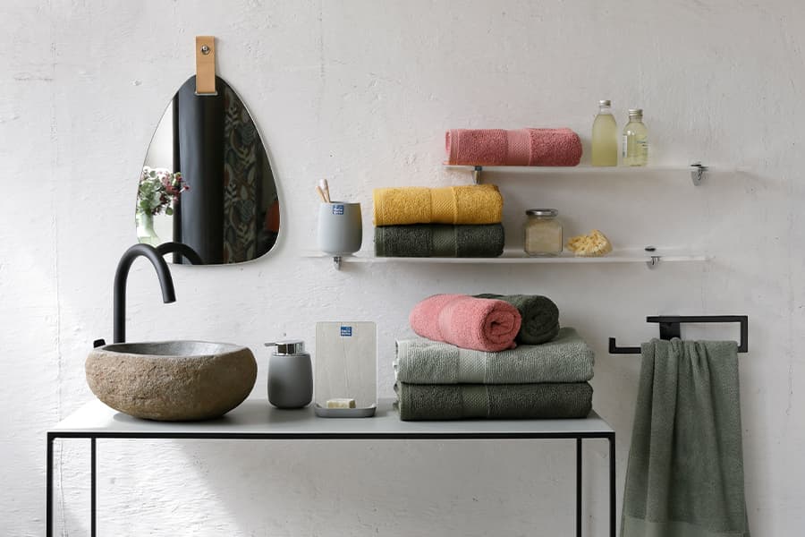 Moderner Waschtisch mit Naturstein-Waschbecken, Spiegel und bunten Handtüchern auf Regalen.