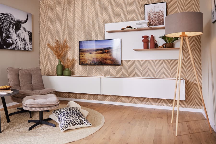 Modernes Wohnzimmer mit Sessel, TV, Stehlampe und dekorativen Regalen. Wand in Zickzack-Muster, Bild eines Hochlandrinds.