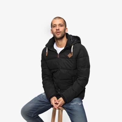 Mann in schwarzer Steppjacke mit Kapuze, sitzt und trägt blaue Jeans