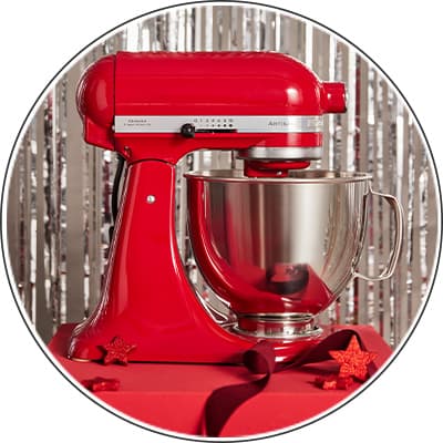 Rot glänzende Küchenmaschine auf rotem Tisch mit Sternen-Dekoration und silbernem Hintergrund