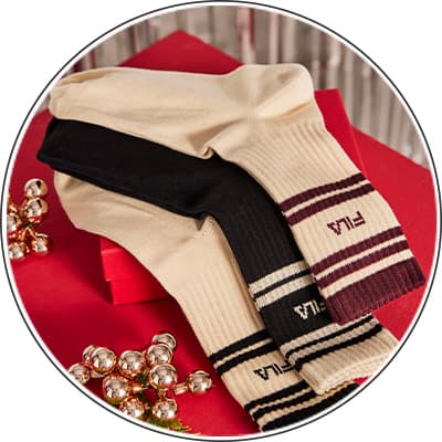 Drei Paar Socken – ein schwarzes und zwei beige mit FILA-Logo, auf rotem Geschenkpapier, daneben Weihnachtsdekoration