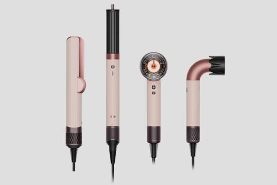 Vier Haarstyling-Geräte in Rosa und Kupfer, darunter ein Lockenstab, eine Rundbürste, ein Föhn und ein Volumizer-Aufsatz