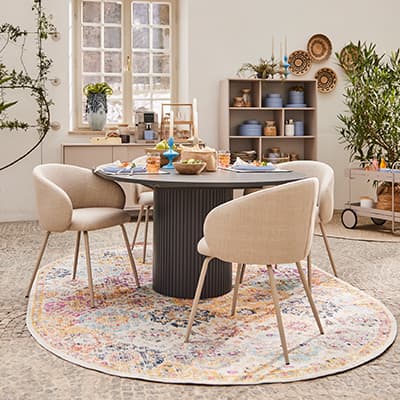 Runder Tisch mit vier beigen Stühlen auf buntem Teppich in gemütlicher Esszimmeratmosphäre