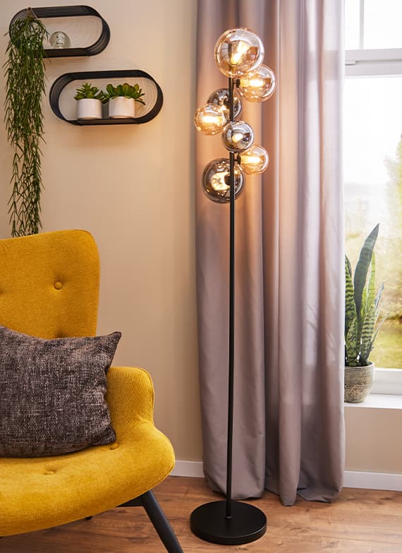 Modernes Wohnzimmer mit gelber Sessel, Stehlampe mit Glaskugeln, grauen Vorhängen und Pflanzen auf Fensterbank und Wandregal.