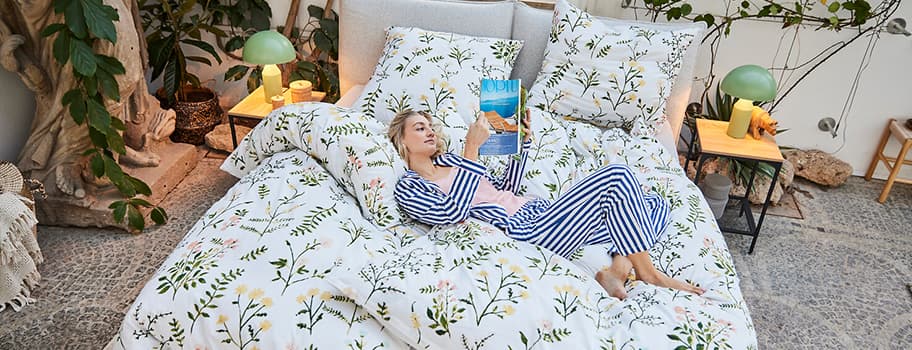 Frau in blau-weiß gestreifter Pyjama liest auf Bett mit blumiger Bettwäsche.